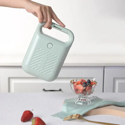 Mint green portable hand warmer above a bowl of fruit near a Sandwich Maker Panini