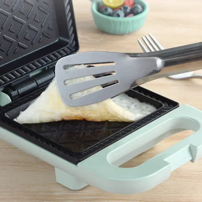 Black waffle maker with mint green handle cooking in Electric Sandwich Maker Panini Press